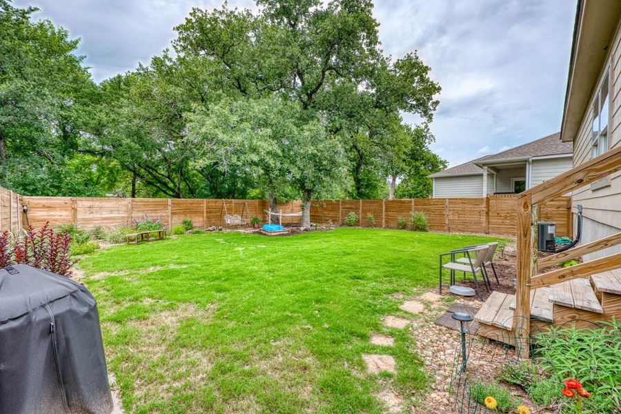 Expansive grassy backyard featuring a natural wood privacy fence, established trees, and a wooden deck with stairs