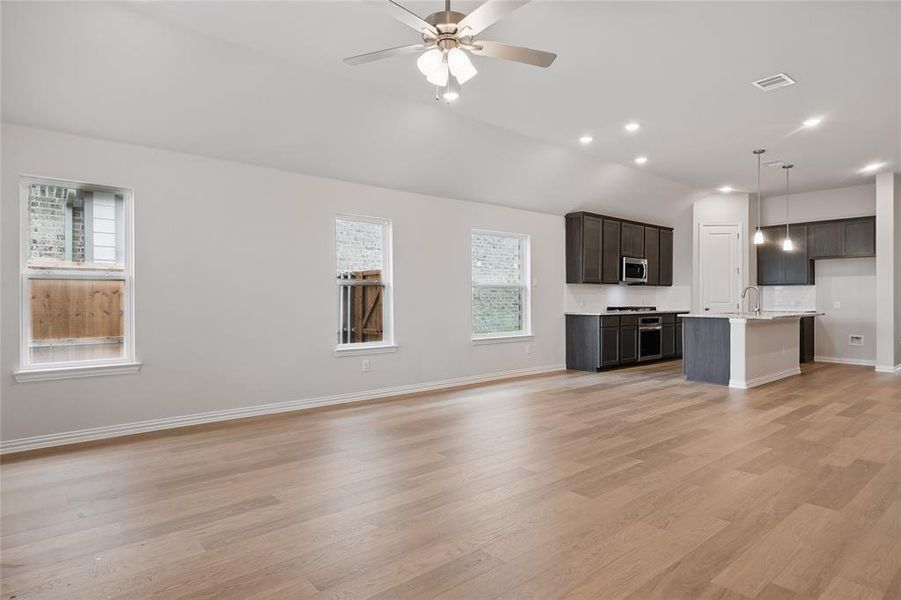 Unfurnished living room featuring vaulted ceiling, light wood-type flooring, baseboards, ceiling fan, and a sink Unfurnished living room featuring vaulted ceiling, light wood-type flooring, baseboards, ceiling fan, and a sink