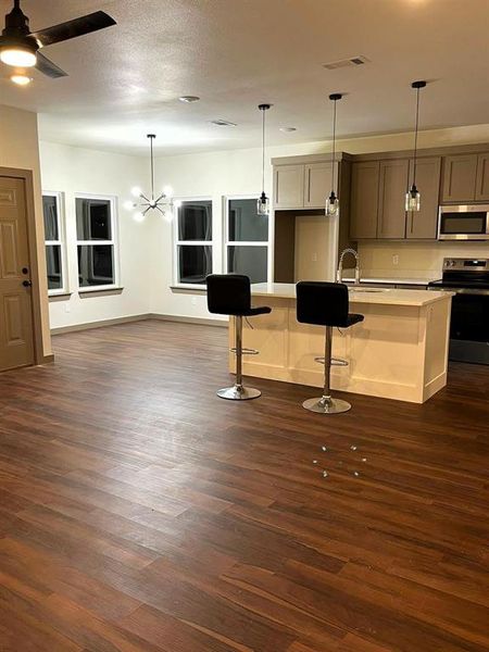 Kitchen with stainless steel appliances, pendant lighting, dark wood-style flooring, a kitchen breakfast bar, and a chandelier Kitchen with stainless steel appliances, pendant lighting, dark wood-style flooring, a kitchen breakfast bar, and a chandelier