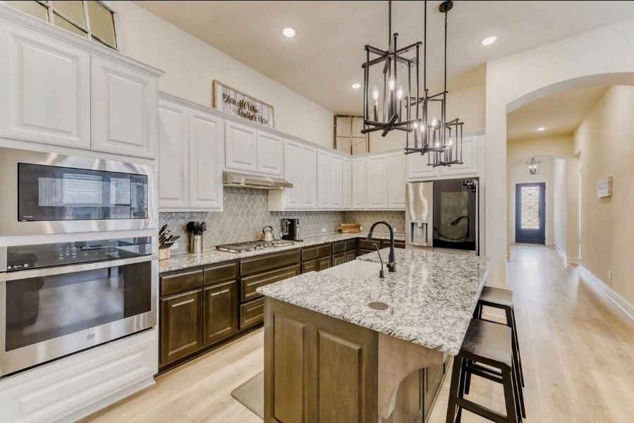 Kitchen with arched walkways, a breakfast bar area, hanging lights, light wood finished floors, and stainless steel appliances