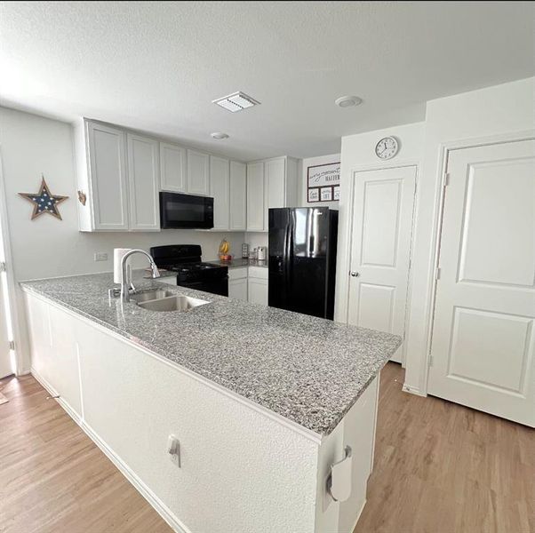 Kitchen featuring black appliances, light wood-style floors, white cabinets, a peninsula, and light stone countertops Kitchen featuring black appliances, light wood-style floors, white cabinets, a peninsula, and light stone countertops