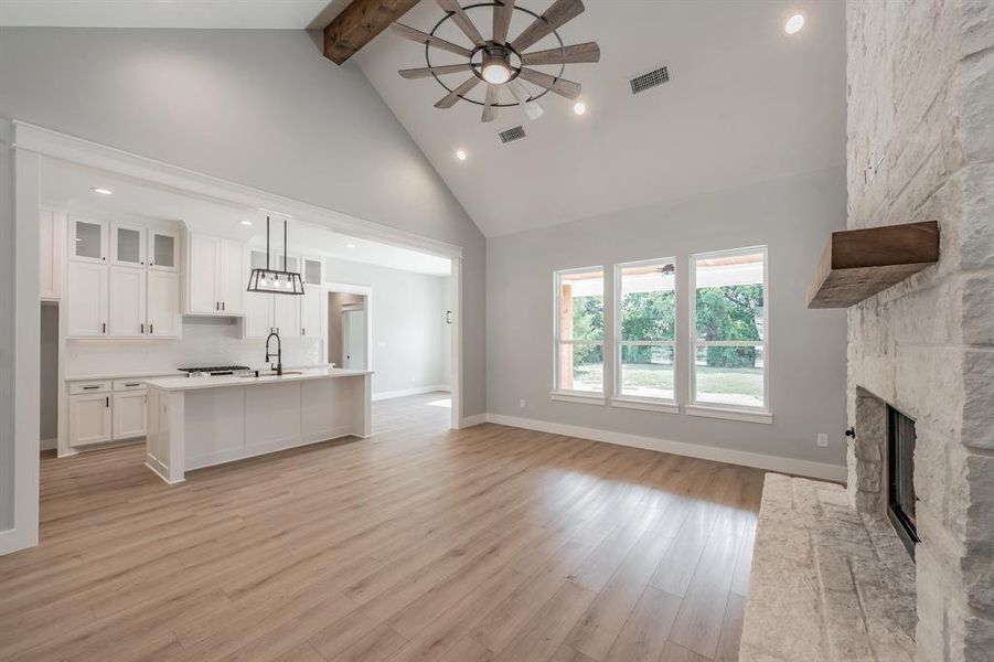 Unfurnished living room with beam ceiling, high vaulted ceiling, a fireplace, and light wood-type flooring