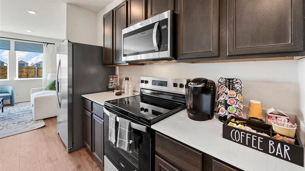 Kitchen featuring dark brown cabinets, stainless steel appliances, light wood finished floors, light stone counters, and recessed lighting