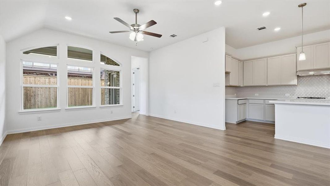 Open-concept living space featuring wood-finish flooring, a vaulted ceiling, and an integrated kitchen Open-concept living space featuring wood-finish flooring, a vaulted ceiling, and an integrated kitchen