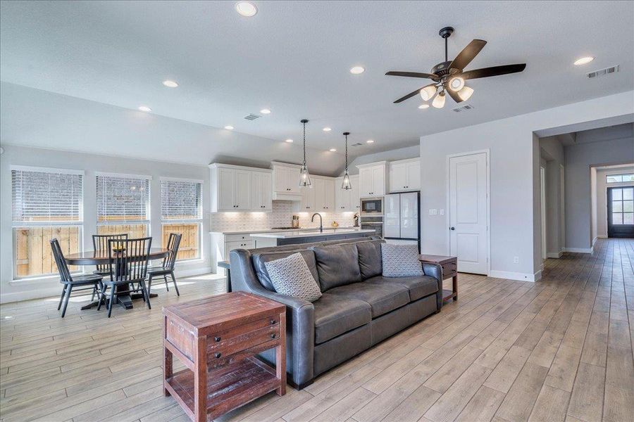 Living area featuring light wood-type flooring, a ceiling fan, vaulted ceiling, and recessed lighting