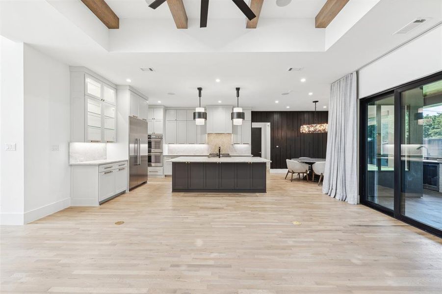 Kitchen featuring white cabinetry, pendant lighting, an island with sink, beam ceiling, and light hardwood / wood-style flooring