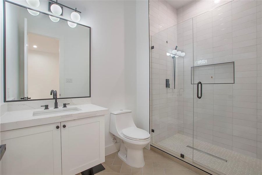 Bathroom featuring toilet, vanity, tile patterned floors, and a shower with door