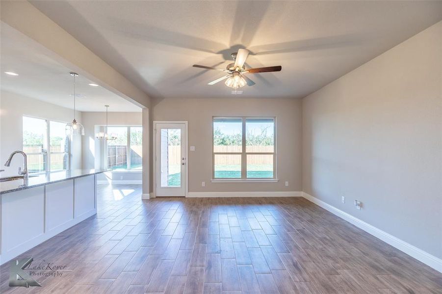 Unfurnished living room with wood tiled floors, a chandelier, healthy amount of natural light, ceiling fan, and recessed lighting