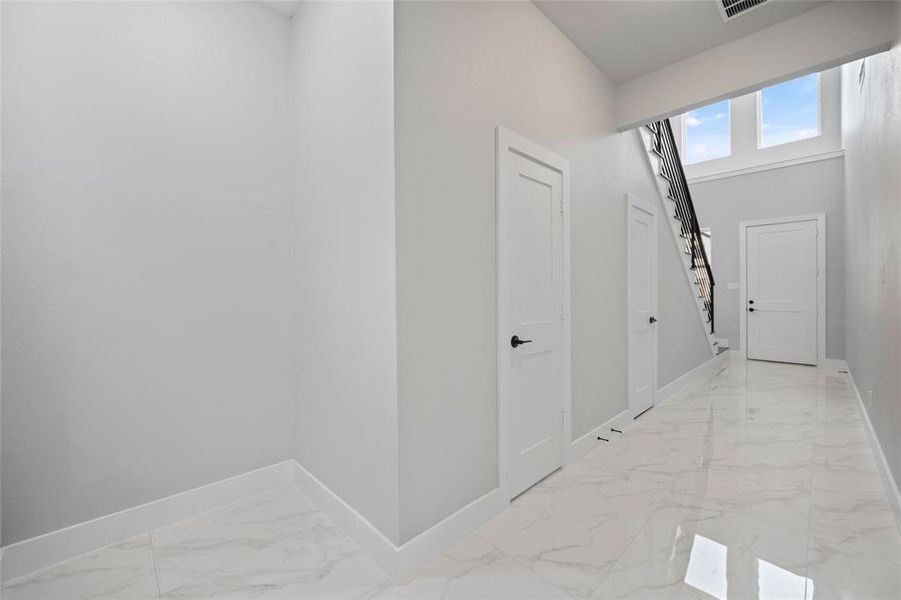 Corridor with visible vents, marble finish floor, baseboards, and a towering ceiling