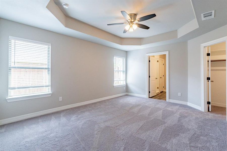 Primary bedroom featuring a walk in closet, ceiling fan, a raised ceiling