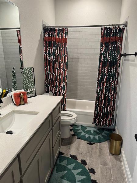 Full bathroom featuring a textured wall, shower / bathtub combination with curtain, vanity, and wood finish floors Full bathroom featuring a textured wall, shower / bathtub combination with curtain, vanity, and wood finish floors