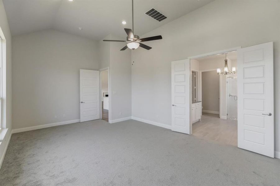 Unfurnished bedroom with ensuite bathroom, high vaulted ceiling, carpet, and ceiling fan with notable chandelier