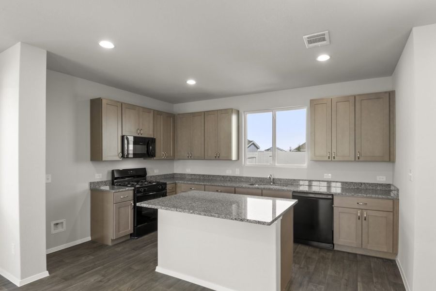 Image of a kitchen with a granite counter top center island, light brown cabinets, black appliances and a window above the sink