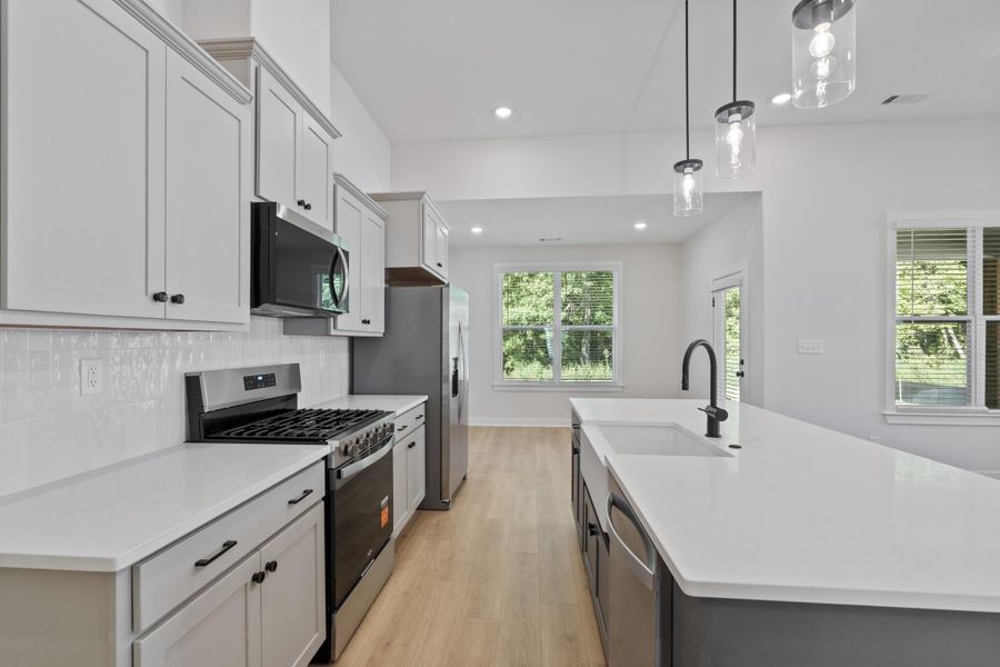 Modern kitchen featuring light cabinetry, stainless steel appliances, a white tile backsplash, and a large island with an integrated sink