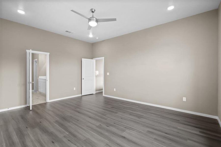 Unfurnished bedroom featuring connected bathroom, dark wood-type flooring, and ceiling fan