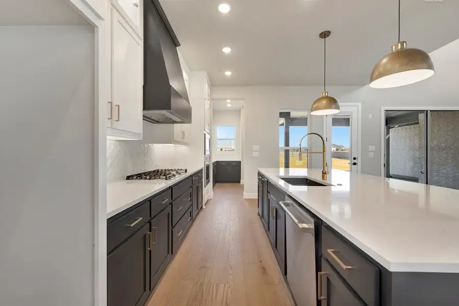 Kitchen with dual tone cabinetry, light wood-style floors, decorative light fixtures, a large island, and stainless steel appliances Kitchen with dual tone cabinetry, light wood-style floors, decorative light fixtures, a large island, and stainless steel appliances