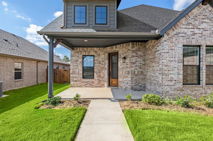 Property entrance featuring brick siding, a shingled roof, and covered porch