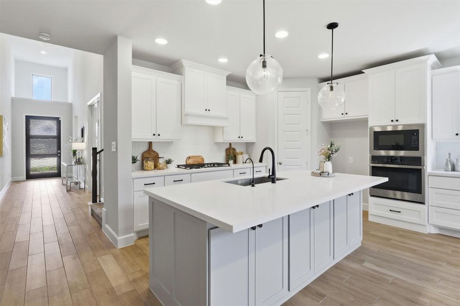 This stunning perspective showcases the kitchen's seamless connection to the home's impressive entry and living spaces. Designer globe pendant lighting, soaring ceilings, stainless steel appliances, and timeless finishes create a space that's equally beautiful and practical.