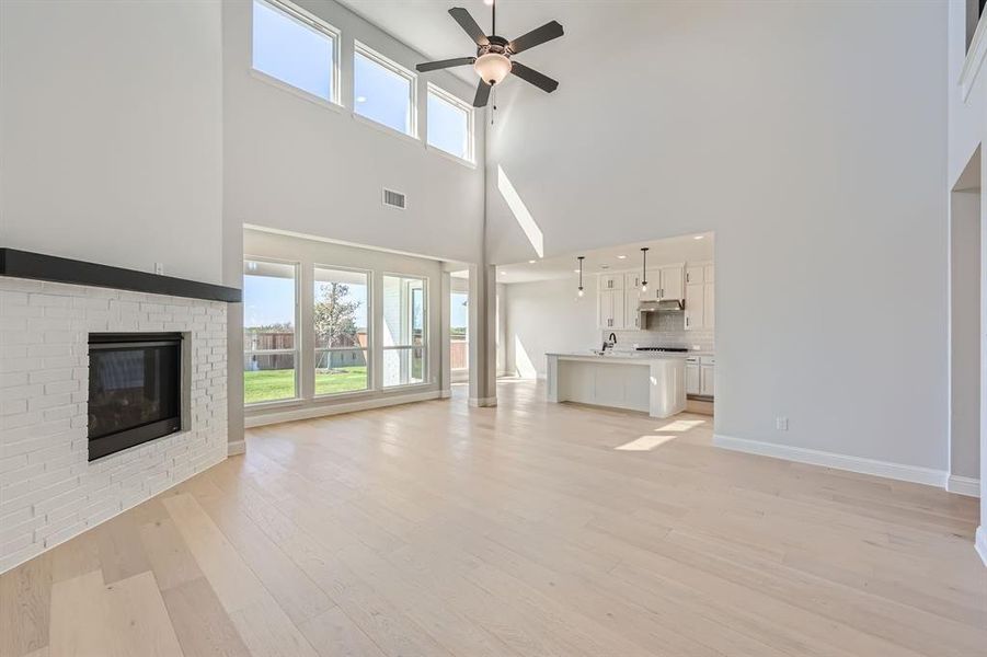 Unfurnished living room featuring a brick fireplace, light hardwood / wood-style floors, a high ceiling, and ceiling fan