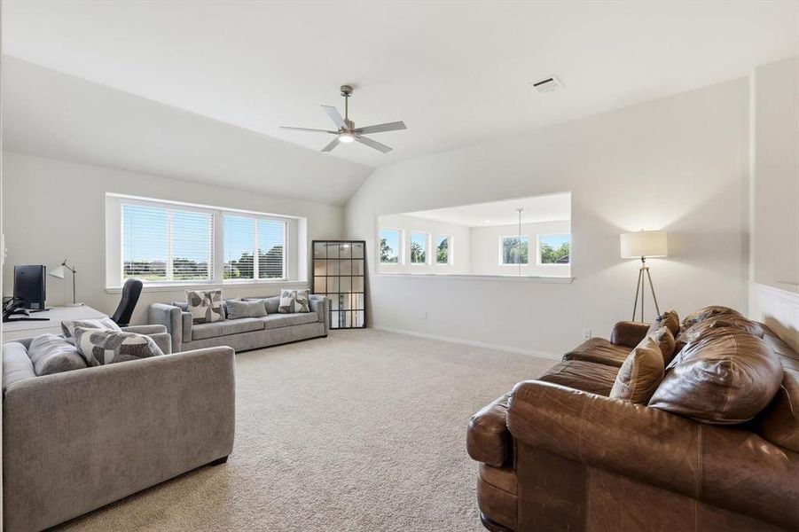 Spacious room featuring vaulted ceilings, light-colored carpeting, and an integrated ceiling fan