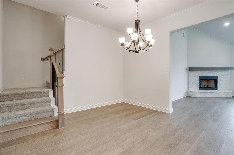 Unfurnished living room featuring an inviting chandelier, crown molding, a brick fireplace, and hardwood / wood-style floors