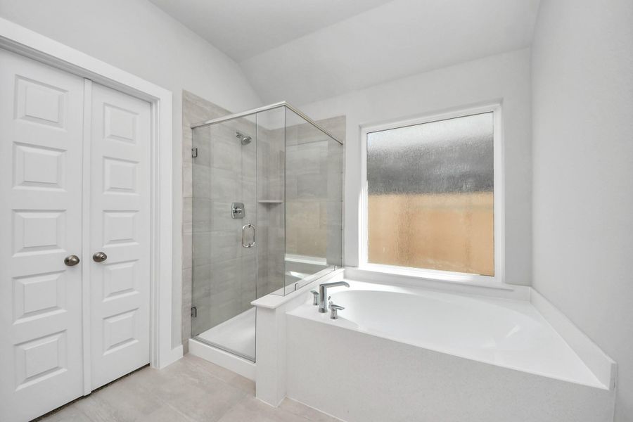 Indulge in a spa-like retreat within the confines of this primary bathroom. Delight in a spacious walk-in shower enveloped in stylish tile surround, unwind in a separate garden tub adorned with custom detailing. Sample photo of completed home with similar floor plan. Actual colors and selections may vary.
