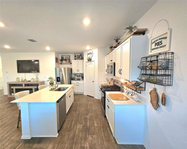 Open-concept kitchen featuring an island with a built-in sink and seating, stainless steel appliances, white cabinetry, and wood-finish flooring