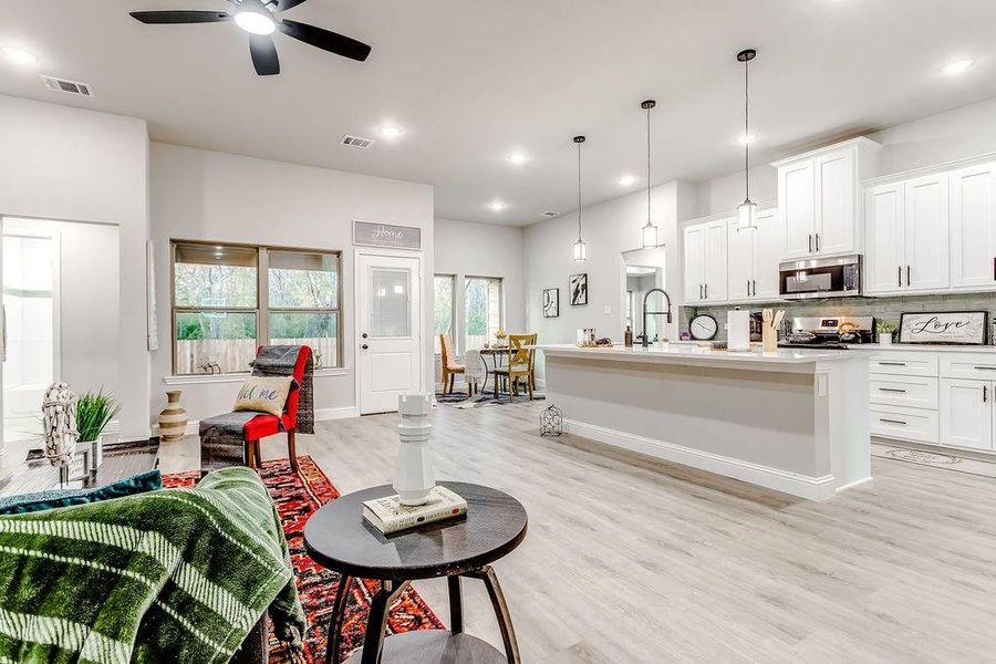 Kitchen with white cabinets, a center island with sink, hanging light fixtures, ceiling fan, and stainless steel appliances