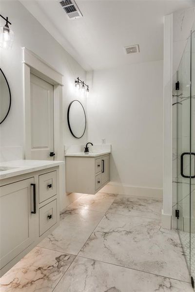 Bathroom featuring light marble finish flooring, two vanities, and a marble finish shower Bathroom featuring light marble finish flooring, two vanities, and a marble finish shower