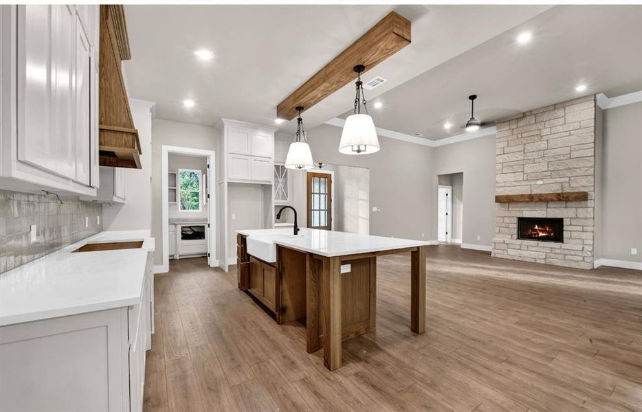 Kitchen with white cabinetry, beamed ceiling, a stone fireplace, decorative light fixtures, and light wood-style floors