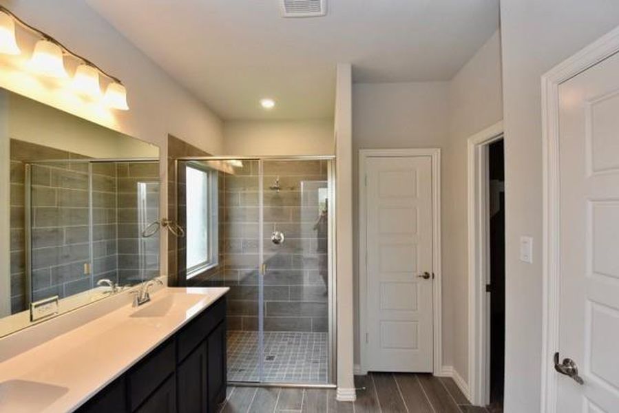 Full bathroom featuring a stall shower, double vanity, and wood finished floors Full bathroom featuring a stall shower, double vanity, and wood finished floors