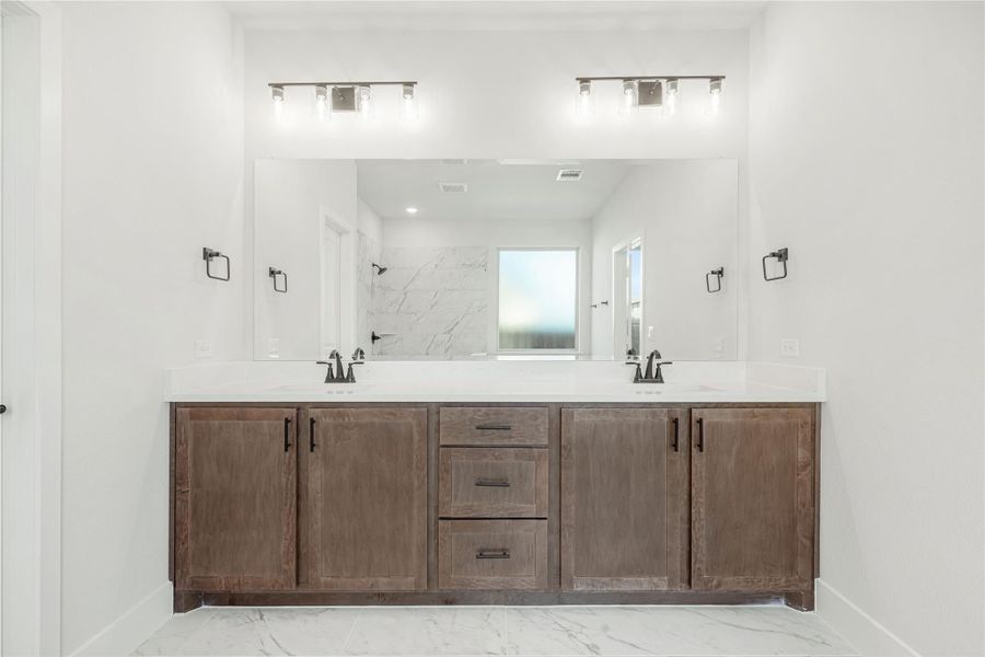 Bathroom with double-sink vanity, wood cabinets, white countertop, and large mirror with wall lights above Bathroom with double-sink vanity, wood cabinets, white countertop, and large mirror with wall lights above