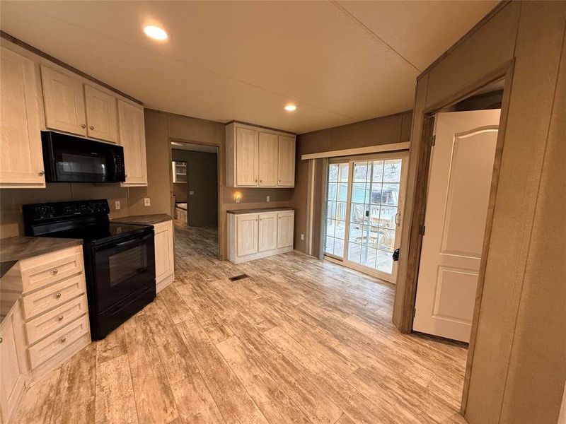 Kitchen with black appliances, light wood-style flooring, recessed lighting, dark countertops, and light wood finish cabinetry