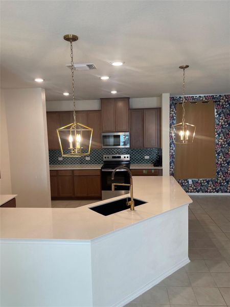 Kitchen featuring a chandelier, light tile patterned floors, appliances with stainless steel finishes, pendant lighting, and backsplash Kitchen featuring a chandelier, light tile patterned floors, appliances with stainless steel finishes, pendant lighting, and backsplash