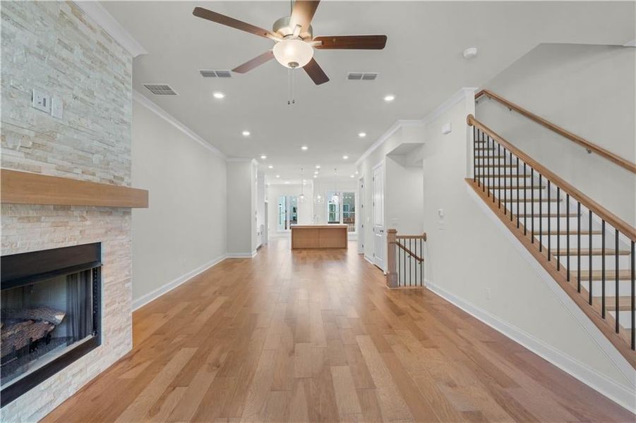 Unfurnished living room featuring ornamental molding, light wood-style floors, a stone fireplace, recessed lighting, and a ceiling fan
