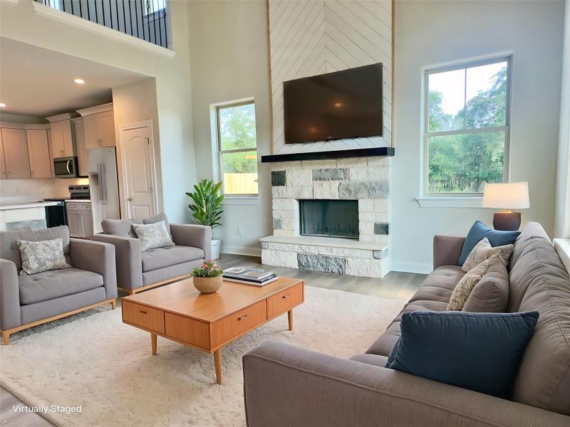 Living area featuring light wood-style flooring, plenty of natural light, a towering ceiling, a stone fireplace, and recessed lighting. Virtually Staged Living area featuring light wood-style flooring, plenty of natural light, a towering ceiling, a stone fireplace, and recessed lighting. Virtually Staged