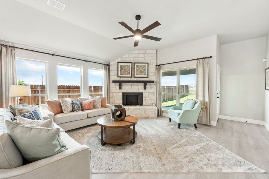 Living room with vaulted ceiling, stone fireplace, ceiling fan, and large windows with backyard views Living room with vaulted ceiling, stone fireplace, ceiling fan, and large windows with backyard views