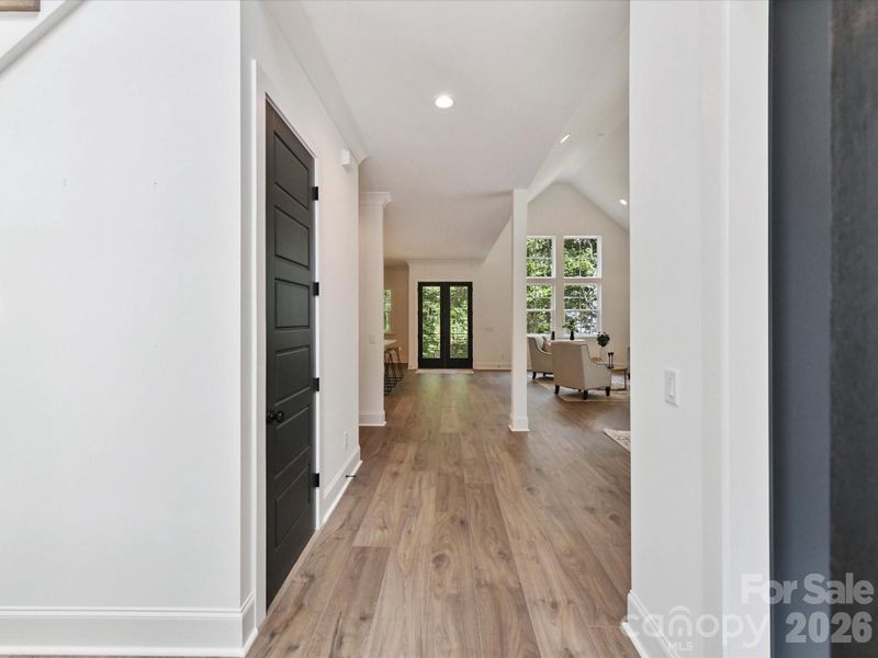 Bright, welcoming entry hall with wide plank flooring, modern black doors, and an open sightline to the light-filled living area with views of the outdoors.