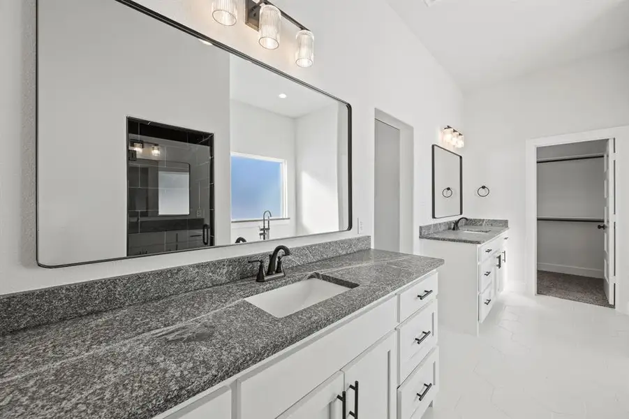 Bathroom with two vanities, a walk in closet, and a stall shower