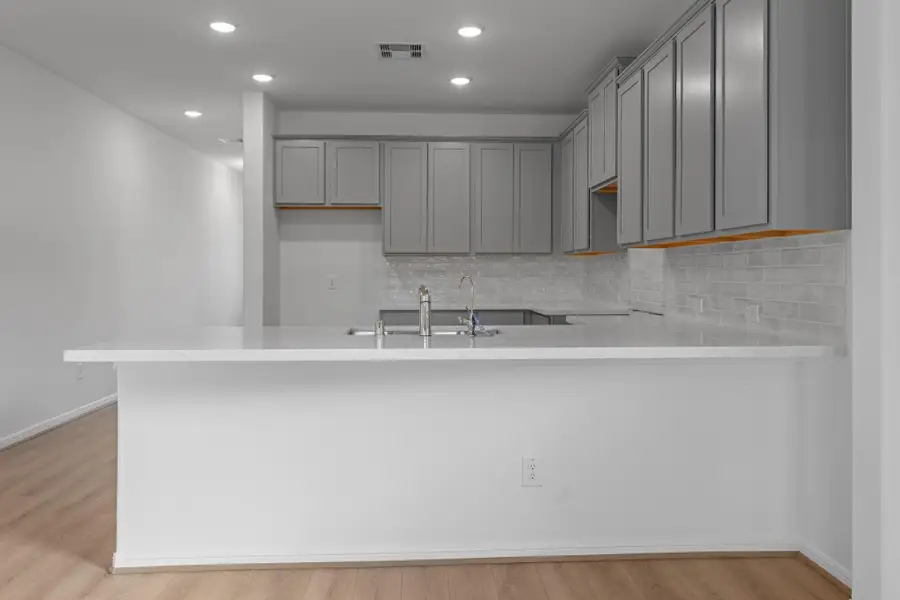 This light and bright kitchen features a large quartz island, white cabinets, a large sink overlooking your family room, recessed lighting, and beautiful backsplash.