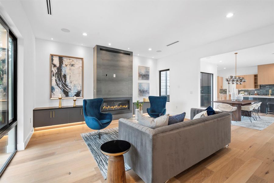 The living area features light hardwood flooring, a modern fireplace with a dark surround, and large windows