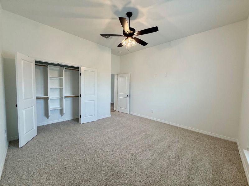 Spacious room featuring neutral carpeting, a dark-toned ceiling fan with integrated lighting, and a closet with bifold doors and built-in shelving