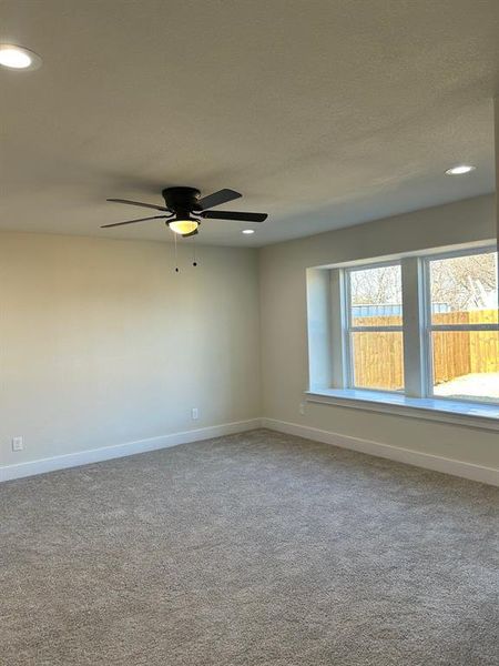 Primary bedroom has carpeted floors, a ceiling fan and large windows for natural light flow