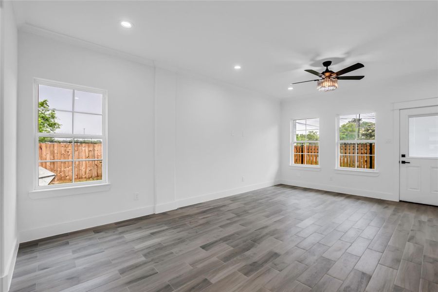 This inviting living room boasts sleek wood floors, abundant natural light through ample windows, and a stylish ceiling fan, creating a perfect blend of comfort and modern elegance.