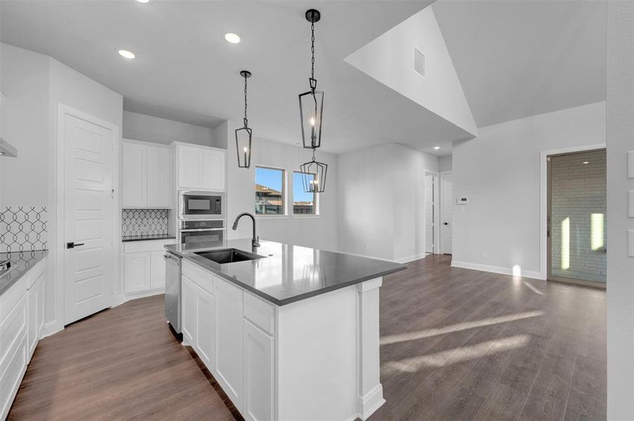 Kitchen with white cabinetry, a kitchen island with sink, decorative backsplash, dark wood-style flooring, and stainless steel appliances Kitchen with white cabinetry, a kitchen island with sink, decorative backsplash, dark wood-style flooring, and stainless steel appliances