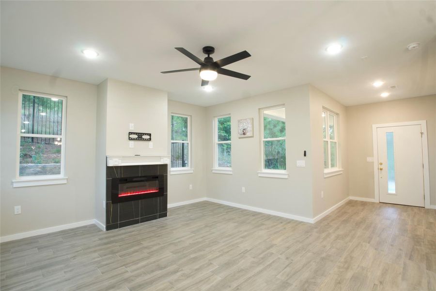 Wide open living room with light wood finished floors, a ceiling fan, a tile fireplace, and recessed lighting.