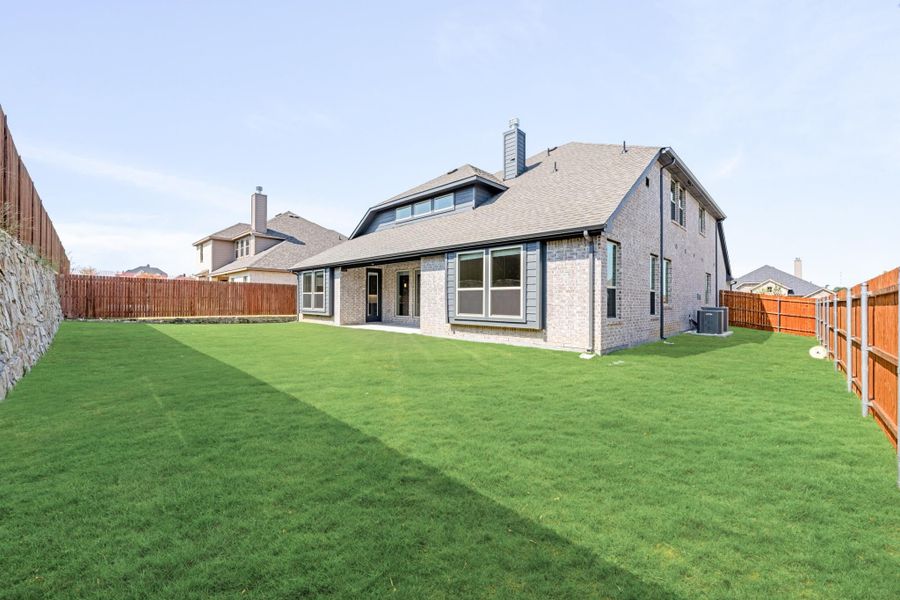 Rear view of two-story brick home with large fenced backyard and green lawn