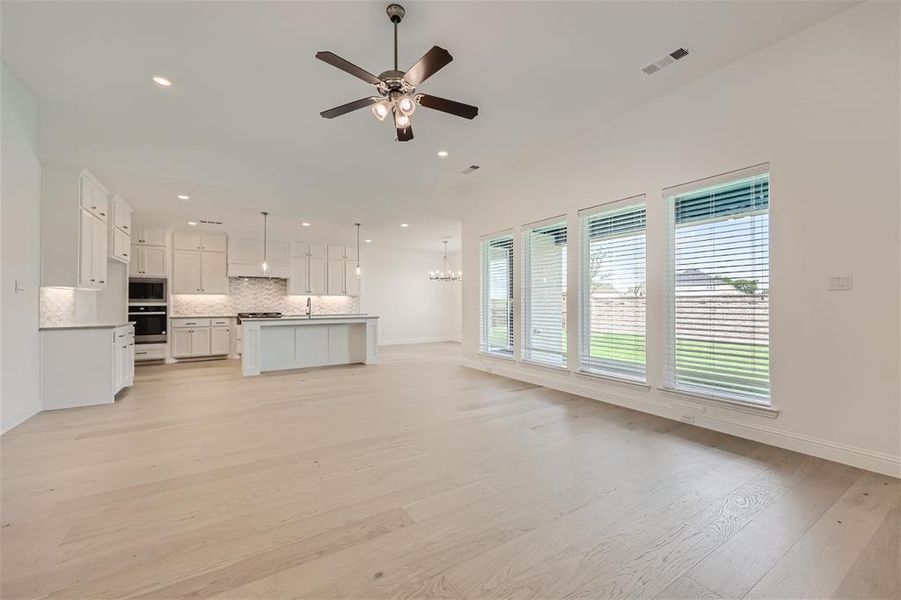 Unfurnished living room featuring light hardwood / wood-style floors, sink, and ceiling fan with notable chandelier