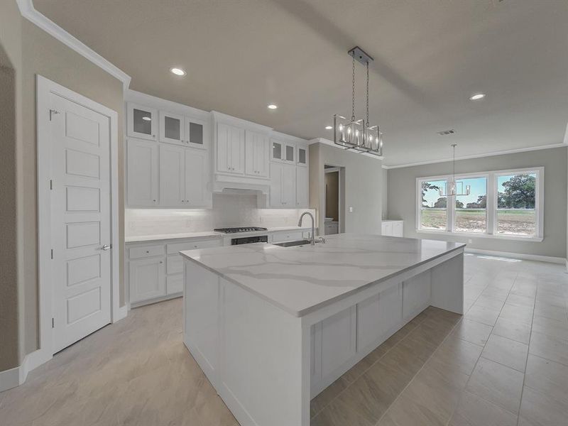 Kitchen with crown molding, white cabinets, a large island with sink, light stone counters, and backsplash Kitchen with crown molding, white cabinets, a large island with sink, light stone counters, and backsplash