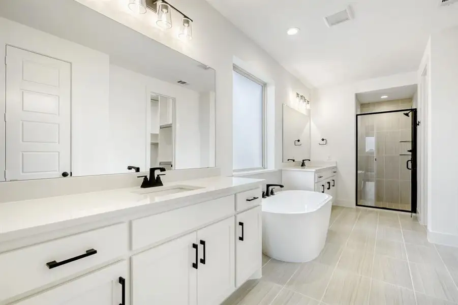 Full bath with a shower stall, two vanities, a freestanding tub, and recessed lighting